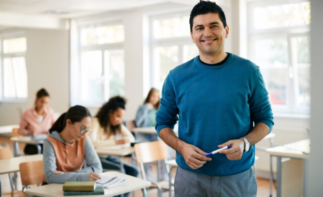 Retrato de professor feliz do ensino médio na sala de aula olhando para a câmera.