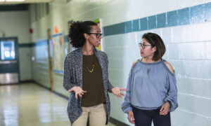 Duas profissionais da escola caminham conversando no corredor da escola.