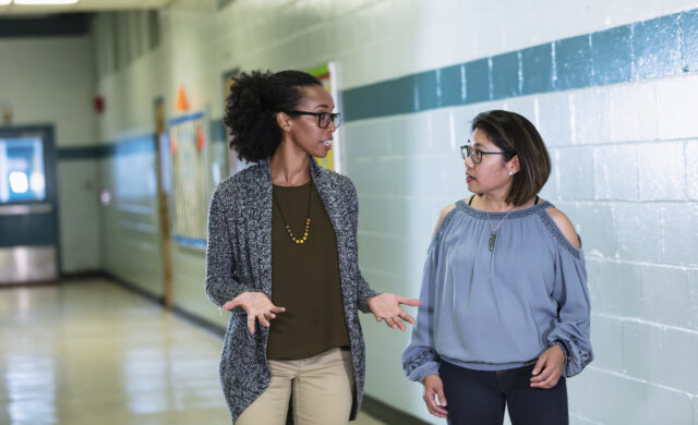 Duas profissionais da escola caminham conversando no corredor da escola.