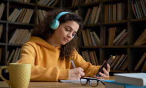 Jovem do ensino médio observa o celular enquanto faz anotações.