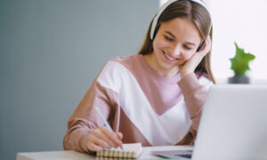Jovem estudante sentada à mesa, usando laptop ao estudar em casa.
