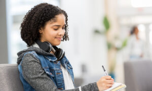 Adolescente sentada no sofá pensativa enquanto faz anotações.