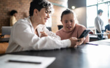 Duas estudantes com deficiência na sala de aula olhando o celular.