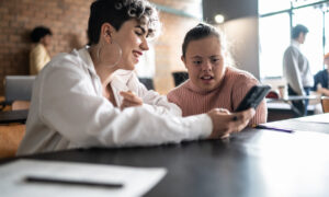 Duas estudantes com deficiência na sala de aula olhando o celular.